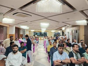 Community members attending a Jain Samiti event in a decorated hall with chandeliers, seated in rows, participating in a cultural and spiritual gathering.