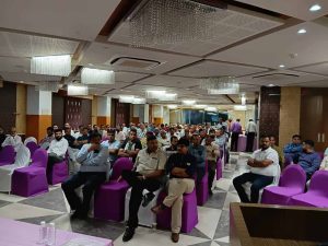 Audience seated on purple chairs during a Jain Samiti community event in Ahmedabad, attentively listening to discussions in a well-lit hall with chandeliers.