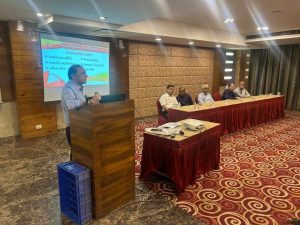 Speaker addressing the audience during a Dariyapuri Sthanakwasi Jain Samiti event in Ahmedabad, with committee members seated on stage and a presentation screen in the background.