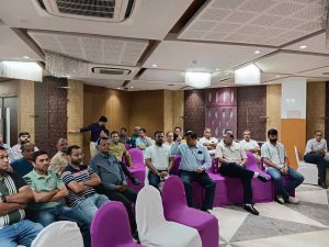 Community members of Dariyapuri Sthanakwasi Jain Samiti are seated on purple chairs during a meeting in Ahmedabad, listening to discussions in a hall